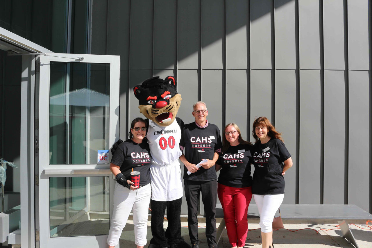 Faculty and the dean stand next to the bearcat and are wearing shirts that say "CAHS."