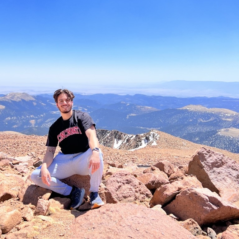 Brenden Benjamin, Second-year DTP student sits on top of a mountain.