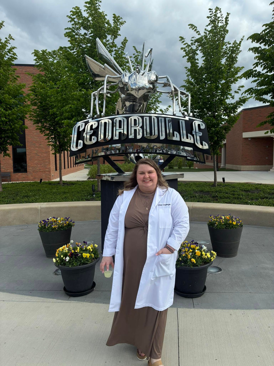 Chloe Caplinger stands in a white coat in front of a statue